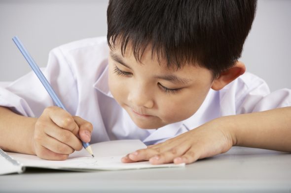 工作在书桌的男学生在中国学校教室